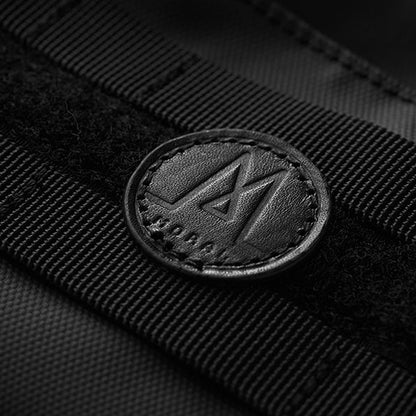 Moral NIGHTHAWKS MILITARY DUO MINI 軍事風側背包品牌標誌特寫，展現細緻的皮革圓形Logo設計。精緻縫線與軍事風織帶，突顯質感與識別度。